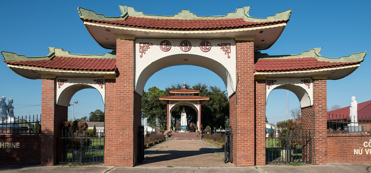 A front view of the Queen of Peace Shrine and Gardens in a largely Vietnamese neighborhood of Port Arthur, Texas. A large, three-part arch framing a garden with statuary inside.